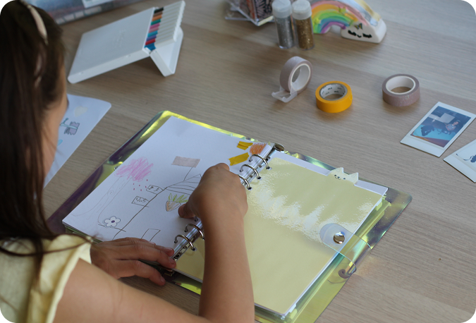 Child drawing in a notebook at a craft table
